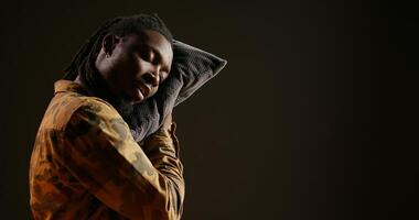 Sleepy person napping with his pillow while he is standing, falling asleep on camera because of burnout and fatigue. Tired african american guy feeling exhausted and overworked, insomnia concept. photo