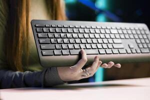 Gen Z girl typing on mechanical keyboard while doing review in personal studio to see if price is justified. Young influencer showcasing computer peripheral features to fans, close up shot photo