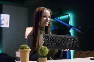 Cheerful content creator analyzing mechanical keyboard received from sponsor, doing honest review for online streaming channel. Internet show host reviewing computer peripherals brand photo