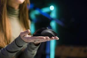 Woman filming for online channel in dimly lit home studio, presenting wireless mouse to fans. Content creator showing audience computer peripheral device, close up shot photo
