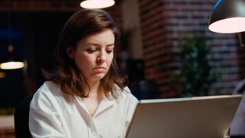 Businesswoman researching key data for company project, doing tasks in office overnight. Employee looking over accounting figures on laptop screen late at night, typing on keyboard, camera B photo