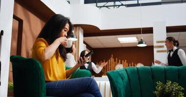 Tourist scrolling social media apps on smartphone, using free wifi connection in lounge area to pass time before doing check in. Asian woman relaxing on couch and planning trip itinerary. photo