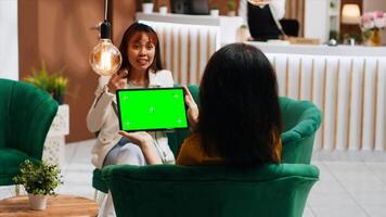 Hotel guest holding tablet with greenscreen layout in lobby, looking at chromakey isolated display and relaxing on sofa. Woman checking blank mockup copyspace screen on gadget. photo