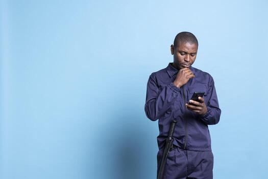 Security agent browsing apps on his smartphone in front of camera, texting messages on work break. Young guarding personnel in uniform checking his social media accounts online. photo
