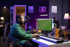 Audio technician creating new tunes on his mixing console, using pc with isolated mockup screen. Producer adjusting volume levels on his recordings to launch new music in his home studio. photo