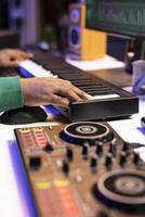 Songwriter playing midi controller synthesizer to record acoustics notes over old audio recordings, editing songs in home studio. Producer working with stereo gear to mix and master tunes. Close up. photo