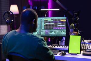 Songwriter composer mixing and mastering tracks next to greenscreen, operating on digital audio pc interface to add sound effects on new recordings. Technician in home studio. photo