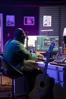 Audio engineer working in home studio with digital software on pc, playing piano keys and editing audio recordings. Musician producer creating tracks on midi controller keyboard notes. photo
