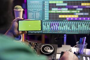 Music producer operating on daw software in home studio and using an isolated display on smartphone, working on new songs. Professional technician adjusting volume levels with mixing console. photo