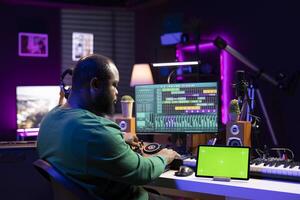 Professional sound engineer editing his music to enhance sound quality, using a greenscreen on tablet. Producer mixing and mastering tunes in his home studio, acoustical engineering. photo