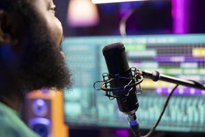 Male composer recording his melody on microphone in home studio, singing a song of his own creation. Talented artist using his audio files and lyrics to apply mixing and mastering techniques. photo