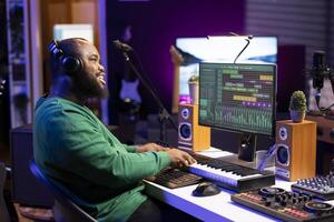 Skilled composer playing piano electronic keyboard to create new music, mixing tunes on digital software to compose a song. Musician adjusting volume levels with pre amp knobs, midi controller. photo