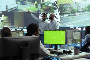 African american employee monitoring delivery trucks on CCTV cameras, using a greenscreen display in control center. Dispatch operator uses gps tracking satellite map, traffic radar. photo