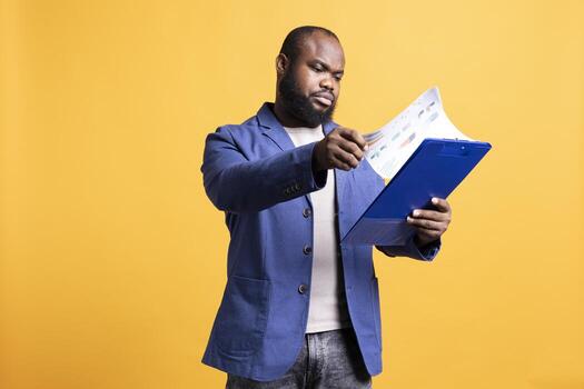 BIPOC person browsing though marketing report pages, studio background. Office clerk reading clipboard with documents containing economic graphs and figures, solving business tasks photo