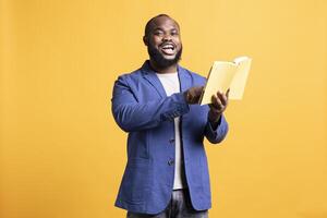 Man laughing while reading funny book, entertained by engrossing story. Happy person having fun, being amused by literature novel during leisure time in studio background photo
