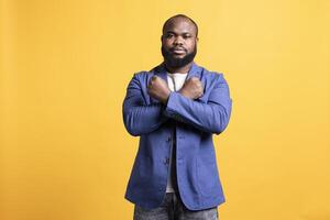 Assertive african american man showing letter X with arms crossed, staying in warrior stance, showing fierceness. Firm BIPOC person using negative body language to signal rejection, studio background photo