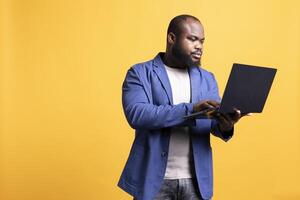 Man looking at business diagram and figures on laptop, isolated over studio background. BIPOC employee checking company financial annual report charts on notebook screen photo