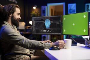 Programmer being greeted by awaken AI gaining consciousness on chroma key computer monitor. Man communicating with artificial intelligence through green screen desktop PC photo