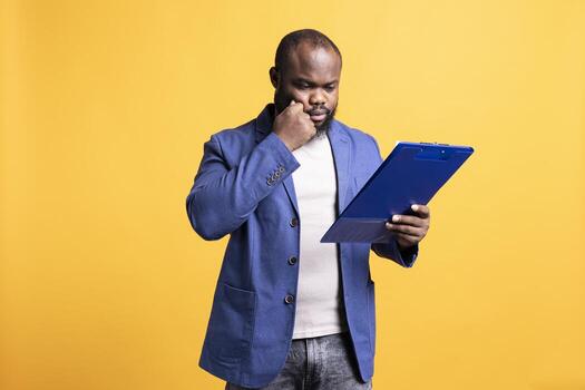 African american man browsing though financial report pages, isolated over studio background. Worker reading clipboard with files containing economic graphs and figures, solving business tasks photo