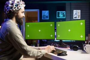 Happy developer using EEG headset device translating thoughts into isolated screen desktop PC commands. Smiling IT specialist controlling mockup multi monitor computer functions using mind photo