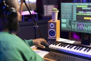Music engineer adding synthesizer notes over his audio files in home studio, editing tracks with digital software and producing new songs for an album. Artist works with mixing console and gear. photo