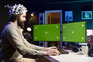 Neuroscientist using EEG headset and isolated screen multi monitor setup to upload mind into computer. Engineer using chroma key PC, experimenting with transferring consciousness into cyberspace photo