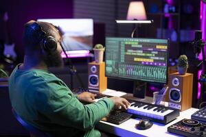 Audio engineer producing a melody by mixing and mastering tunes on stereo console, playing piano electronic keyboard to record tracks on software. Producer creating soundtracks with synthesizer. photo