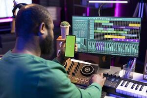 Male technician using mixing console and piano to edit tunes, having isolated mockup screen. Composer producing new music with mixing and mastering techniques in his home studio. photo