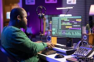 Sound engineer recording piano notes with DAW software in his home studio, working at night on producing new music with electronic tools. Musician composing tunes on midi controller. photo