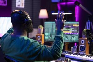 African american skilled audio technician counting down before recording a song, doing a session in his home studio. Producer operating on mixing console and digital software, stereo gear. photo