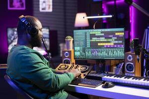 Skilled audio technician mixing and mastering tunes on console, adding sound effects in post production. Songwriter producing new tracks for his album, working in home studio with gear. photo