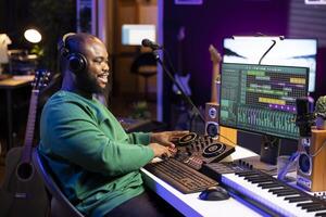 Young musician twisting knobs and mixing tunes with a console, following record settings on a digital software interface. Artist composer producing new music hits in his home studio. photo