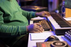 In his home studio, songwriter writes down lines and melodic elements to create new tunes. Using digital audio workstation software, composing and recording songs in post production. photo