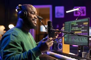 Skilled artist composer singing an acoustic version of his new song, using microphone to record the track and edit in on DAW software interface. Songwriter works on music in home studio. photo