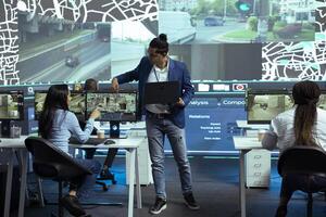 Indian coordinator offers instructions for his staff in control center monitoring room, following delivery trucks with gps coordinates on satellite map. Agency employees provide support for couriers. photo