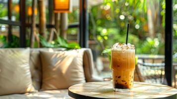 Refreshing glass of Thai iced tea with ice cubes on a cafe table, set against a lush garden background. Classic Thai beverage. Concept of summer drinks, relaxation, tropical atmosphere, Asian culinary photo