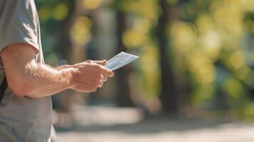 Man holding a document outdoors in a sunny park setting. Close-up of male hand with paperwork. Concept of outdoor work, business on-the-go, document management, and natural light. photo