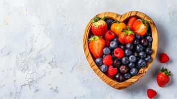 Heart-shaped wooden bowl with assorted berries including strawberries raspberries and blueberries. Fresh colorful fruit mix. Healthy diet, sweet dessert. Banner. Copy space. Foods for healthy heart photo