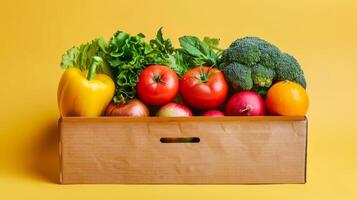 Box of fresh vegetables and fruits on a yellow background. Cardboard box filled with colorful produce. Healthy eating, grocery delivery, fresh food concept photo