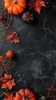 Orange pumpkins and fall leaves on dark background with spider webs. Concept of Halloween, autumn decoration, spooky design, seasonal theme. Copy space. Vertical photo