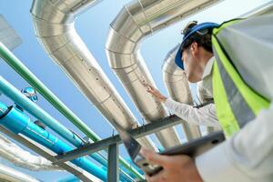 Industrial engineer adjusting pipeline valve with radio communication on construction site. Engineer on urban construction site using radio to coordinate with team on a sunny industrial rooftop. photo