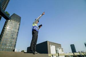 Skilled engineer operating tablet to manage HVAC machinery on top of building, urban architecture in distance. photo