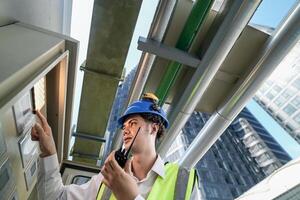 Industrial engineer adjusting pipeline valve with radio communication on construction site. Engineer on urban construction site using radio to coordinate with team on a sunny industrial rooftop. photo