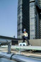 ingeniero en edificio techo con computadora portátil, supervisando urbano construcción, azul cielo, y rascacielos foto