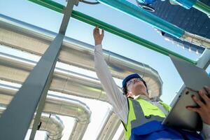 Industrial engineer adjusting pipeline valve with radio communication on construction site. Engineer on urban construction site using radio to coordinate with team on a sunny industrial rooftop. photo
