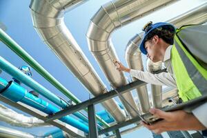 Industrial engineer adjusting pipeline valve with radio communication on construction site. Engineer on urban construction site using radio to coordinate with team on a sunny industrial rooftop. photo