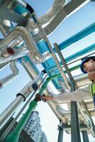 Industrial engineer adjusting pipeline valve with radio communication on construction site. Engineer on urban construction site using radio to coordinate with team on a sunny industrial rooftop. photo