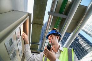 Industrial engineer adjusting pipeline valve with radio communication on construction site. Engineer on urban construction site using radio to coordinate with team on a sunny industrial rooftop. photo