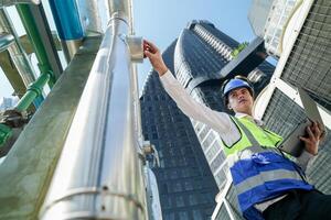 Industrial engineer adjusting pipeline valve with radio communication on construction site. Engineer on urban construction site using radio to coordinate with team on a sunny industrial rooftop. photo