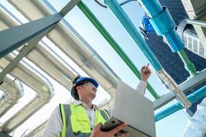 Industrial engineer adjusting pipeline valve with radio communication on construction site. Engineer on urban construction site using radio to coordinate with team on a sunny industrial rooftop. photo